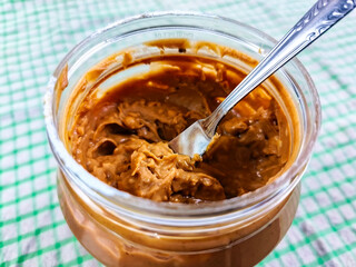 Peanut butter in a jar with a spread knife on top. Peanut butter is very popular to spread on bread to add flavor to the bread. Close up view