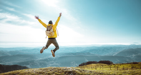 Happy hiker jumping on the top of the mountain at sunset - Man with backpack and arms up standing on the cliff - Happiness and travel concept