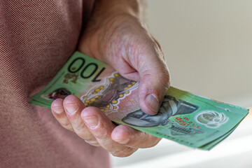 Close-up on a man's hand holding a stack of 100 Australian dollar banknotes.