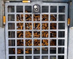 Burnt cigarette butts and rolling tobacco are thrown away in a drop pit container in the ground to prevent litter in nature and on the streets