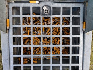 Burnt cigarette butts and rolling tobacco are thrown away in a drop pit container in the ground to prevent litter in nature and on the streets