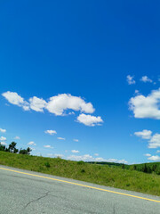 Scenic Roadside View with Vibrant Blue Sky, Fluffy White Clouds, and Lush Green Landscape