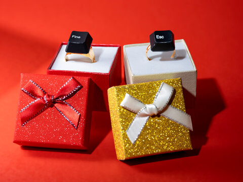 Close-up of two gold rings with computer Esc and Fine keys in gift boxes