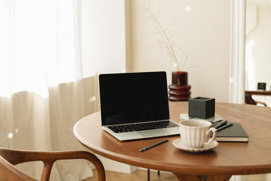 Close-up of a Laptop with a blank screen on a dining table with a cup of coffee and assorted stationery