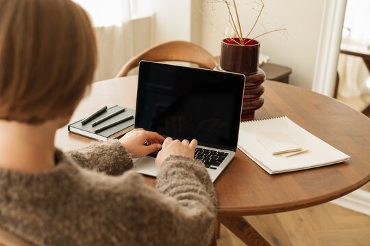 Rear view of a young woman sitting at a dining table using her laptop computer