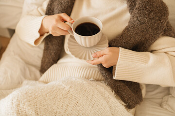 Close-up of a young woman in casual loungewear sitting on her bed drinking morning coffee