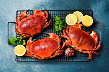 Seafood. Three whole cooked sea crabs laid out on a grill grate. On a gray stone background.