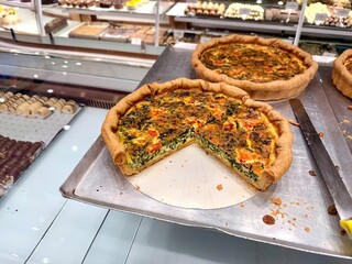 Tasty spinach quiche with tomatoes and cheese at bakery showcase