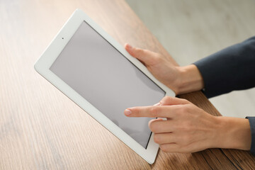 Businesswoman using tablet at wooden table indoors, closeup. Modern technology