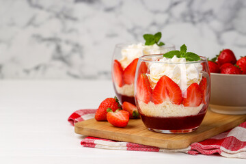 Tasty trifle dessert. Sponge cake, strawberries, jam and whipped cream in glasses on white table