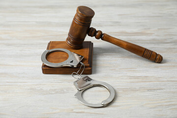Handcuffs and judge's gavel on white wooden table