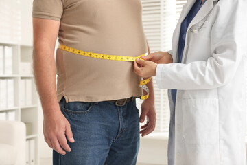 Nutritionist measuring overweight man's waist with tape in clinic, closeup