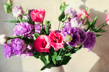 Vase with beautiful eustoma flowers near beige wall, closeup