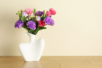 Vase with beautiful eustoma flowers on wooden table, space for text