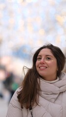 Beautiful woman with long brown hair, in warm winter clothes, standing on a snowy street in winter....