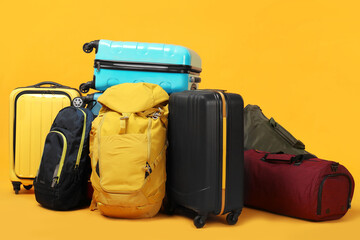 Pile of colorful suitcases, bags and backpacks on orange background