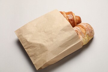 Paper bag with fresh baguette and croissant on light gray table, above view