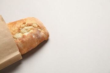 Paper bag with fresh baguette on light gray table, top view. Space for text