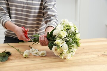 Florist making beautiful wedding bouquet at wooden table indoors, closeup