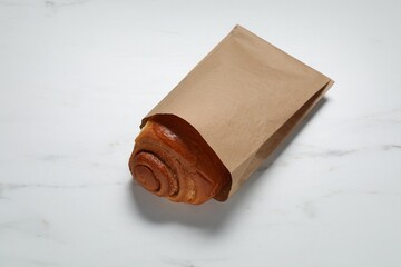 Paper bag with freshly baked bun on white marble table, above view