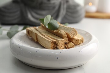 Palo santo sticks and eucalyptus leaves on white table, closeup