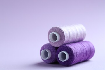 Spools of colorful sewing threads on lilac background, closeup. Space for text