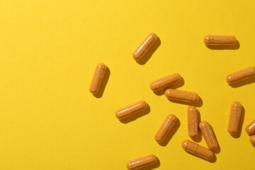 Many turmeric capsules on yellow background, flat lay. Space for text