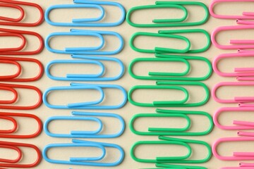 Colorful paper clips on beige background, flat lay