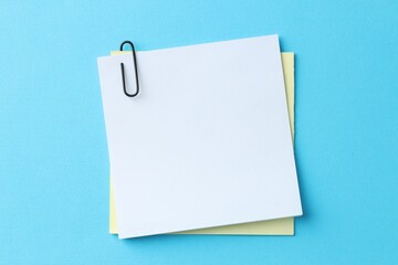 Paper notes with clip on light blue background, top view. Space for text