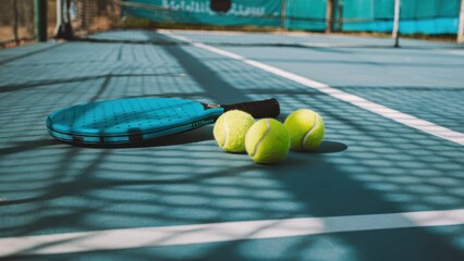 tennis court, close-up view, tennis balls, tennis racket, blue hard court surface, white court lines, net shadow, vibrant colors, sunny day, sports equipment, outdoor tennis, high-contrast lighting, d