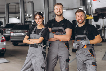 Group of three car service technician men and woman talking at workplace, people working together...