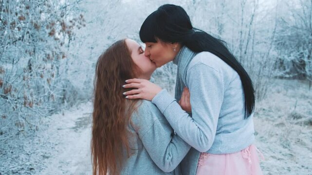 happy family mother and daughter posing kissing hand stroking head hair, woman hugs little girl with love care, two people together. Winter forest trees frost, white snow. Same clothes gray sweater