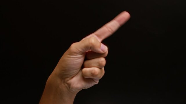 Man pointing with index finger against black background, hand gesture close-up showing direction, communication in dark setting