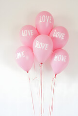 Balloons with the inscription "LOVE" and many balloons of pink and white shades on the background of a white wall. Symbol of Valentine's Day.