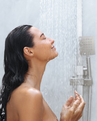 A serene woman with wet hair enjoys a soothing shower with eyes closed, capturing a moment of relaxation and self-care. Perfect for promoting skincare, wellness, and beauty concepts in spa or personal