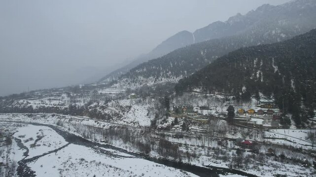 Aerial drone dusk shot showing lit houses on snow covered hillside of liddar Aru valley on the route to Phelgam and a popular rafting point in Kashmir