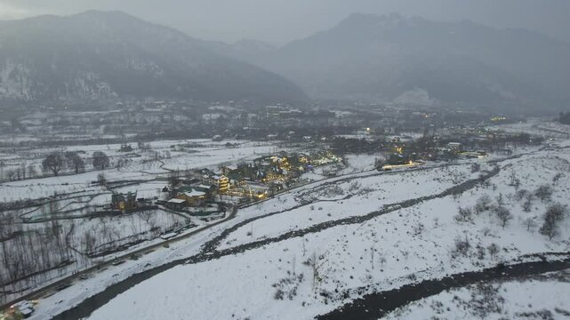 Aerial drone cityscape shot showing lit houses of lidder village near pahalgam srinagar kashmir on riverbank with himalayas in the background