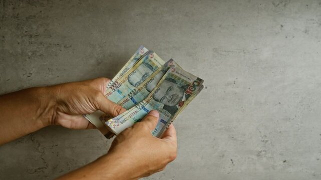 Hands holding and counting peruvian sol banknotes on a gray concrete background