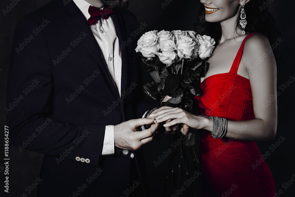 Poster portrait of rich gentleman in tux with bowtie putting on gold ring with diamond on finger to lady je