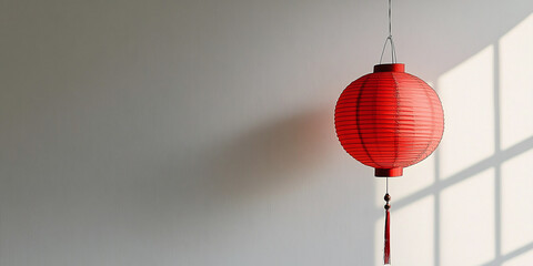 Obraz premium Minimalistic composition featuring a traditional red paper lantern hanging against a plain wall with sunlight casting soft shadows.