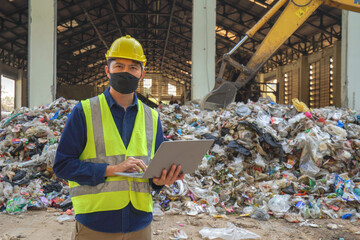 An environmental engineer uses a laptop to check the quality of a landfill in the background while a heavy machinery truck sorts waste at a waste plant.