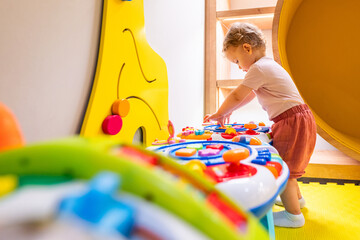 Toddler playing with interactive toy table featuring lights, sounds, and shapes in a play area