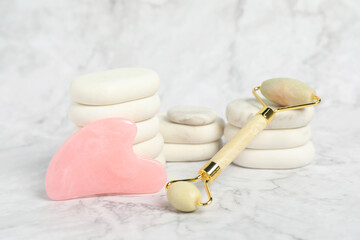 Face roller, gua sha tool and massage stones on white marble background
