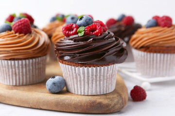 Tasty cupcakes with chocolate cream and berries on white marble table, closeup