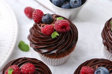 Tasty cupcakes with chocolate cream and berries on white wooden table, closeup