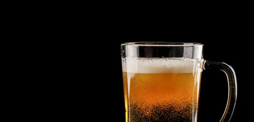 closeup of a single full glass beer mug with foam isolated on black background with copy space and beautiful lighting