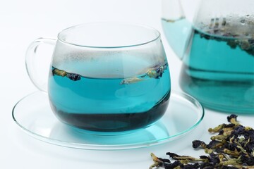 Fresh butterfly pea flower tea in cup and dry petals on white table, closeup