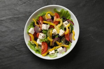 Delicious fresh Greek salad in bowl on black table, top view