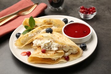Delicious crepes with cottage cheese, jam, redcurrants and blueberries served on grey table, closeup