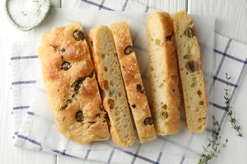 Slices of delicious focaccia bread with olives, thyme and salt on white wooden table, flat lay